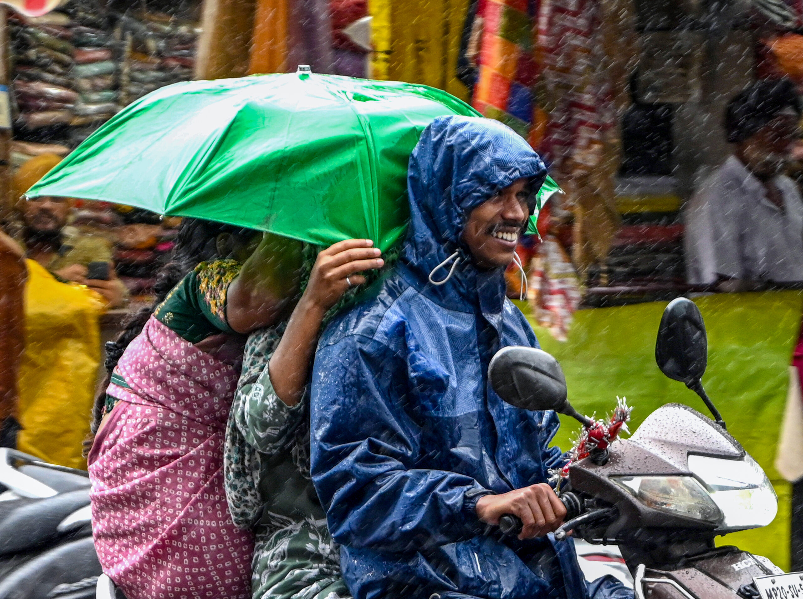 Jabalpur: A family rides a two-wheeler along a city road amid heavy rainfall, with one of them holding an umbrella, in Jabalpur on Wednesday, August 26, 2026. (Photo: IANS)